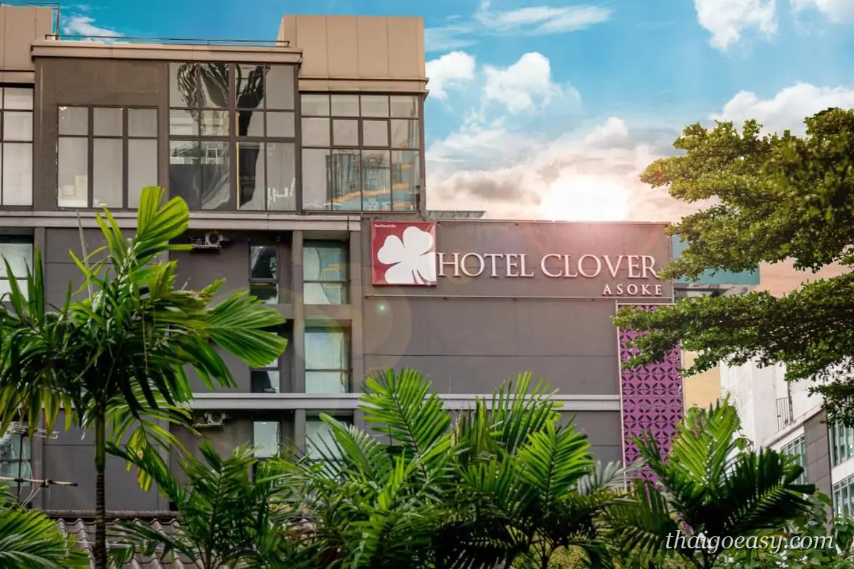 曼谷三葉草阿索克酒店的白色外觀與粉紅色 HOTEL CLOVER ASOKE 招牌，前方是棕櫚樹