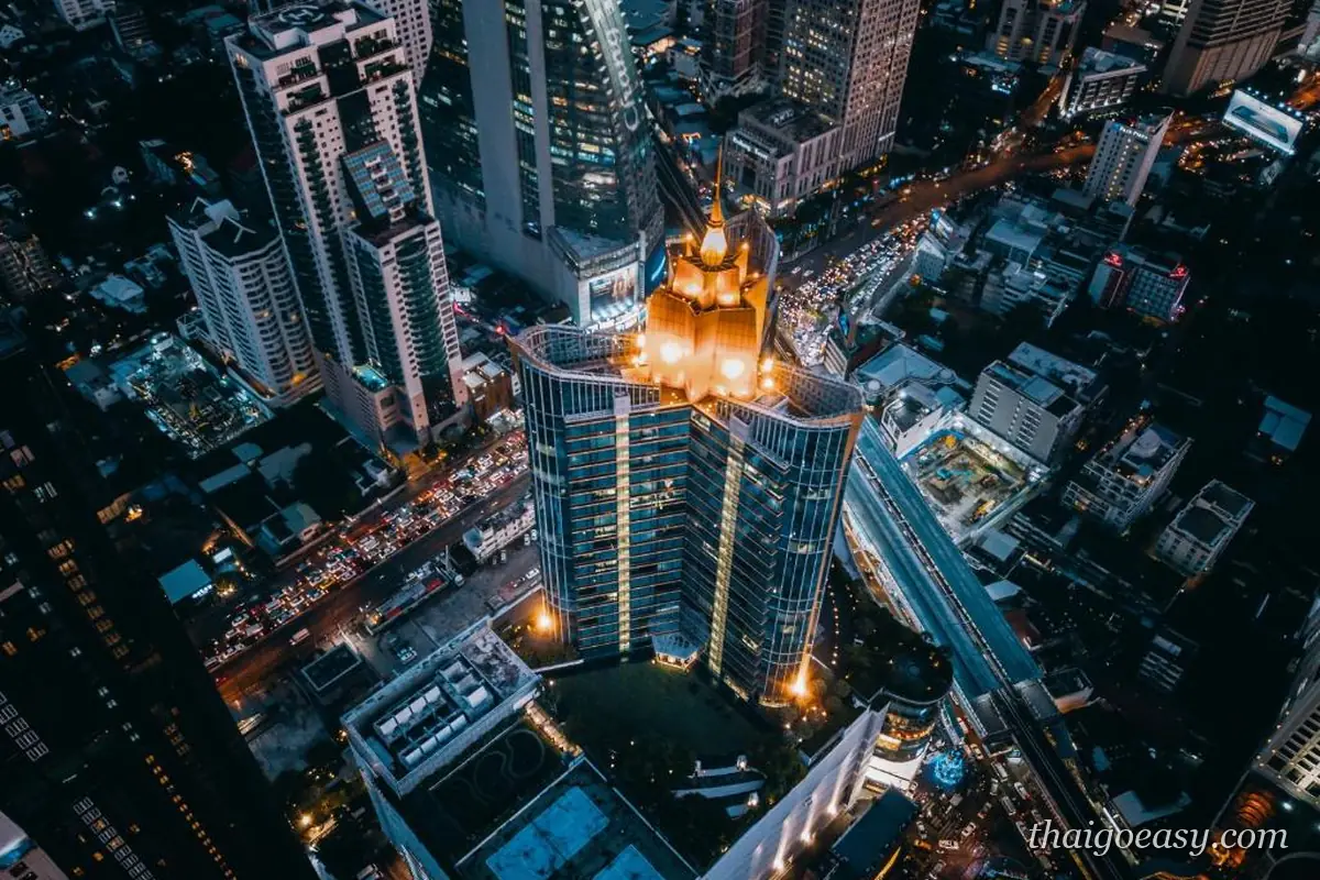 曼谷阿索克空拍夜景，中央高塔頂部打上黃光，四周是密集的商辦高樓