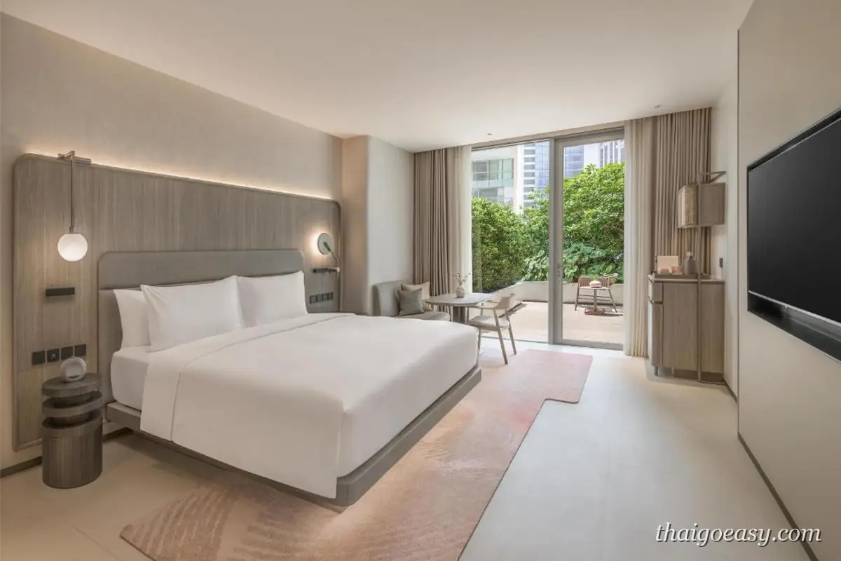 KROMO Bangkok 客房，白色大床與圓形壁燈，落地窗外可見綠樹與陽台