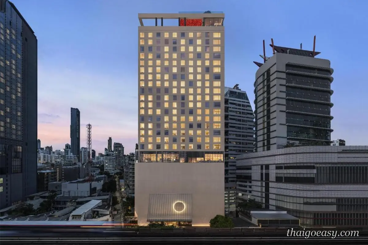 KROMO Bangkok 高樓外觀，黃昏天色下亮起窗燈，周邊是蘇坤蔚高樓