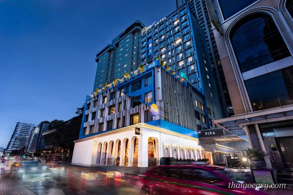 琵帕飯店夜間外觀，白色古典門廊與後方藍色玻璃塔樓，門前是車流燈軌