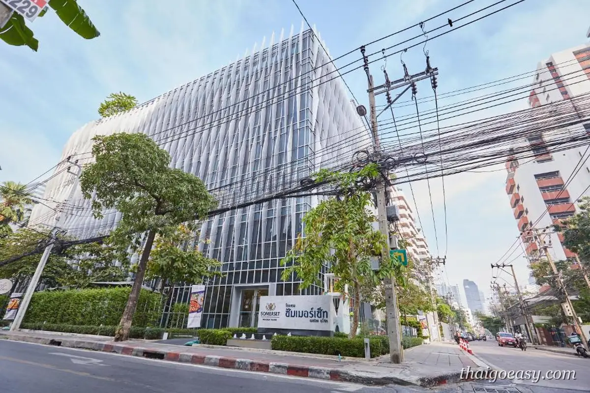 盛捷明軒阿索克公寓酒店所在的街角玻璃帷幕大樓，路旁有行道樹與電線