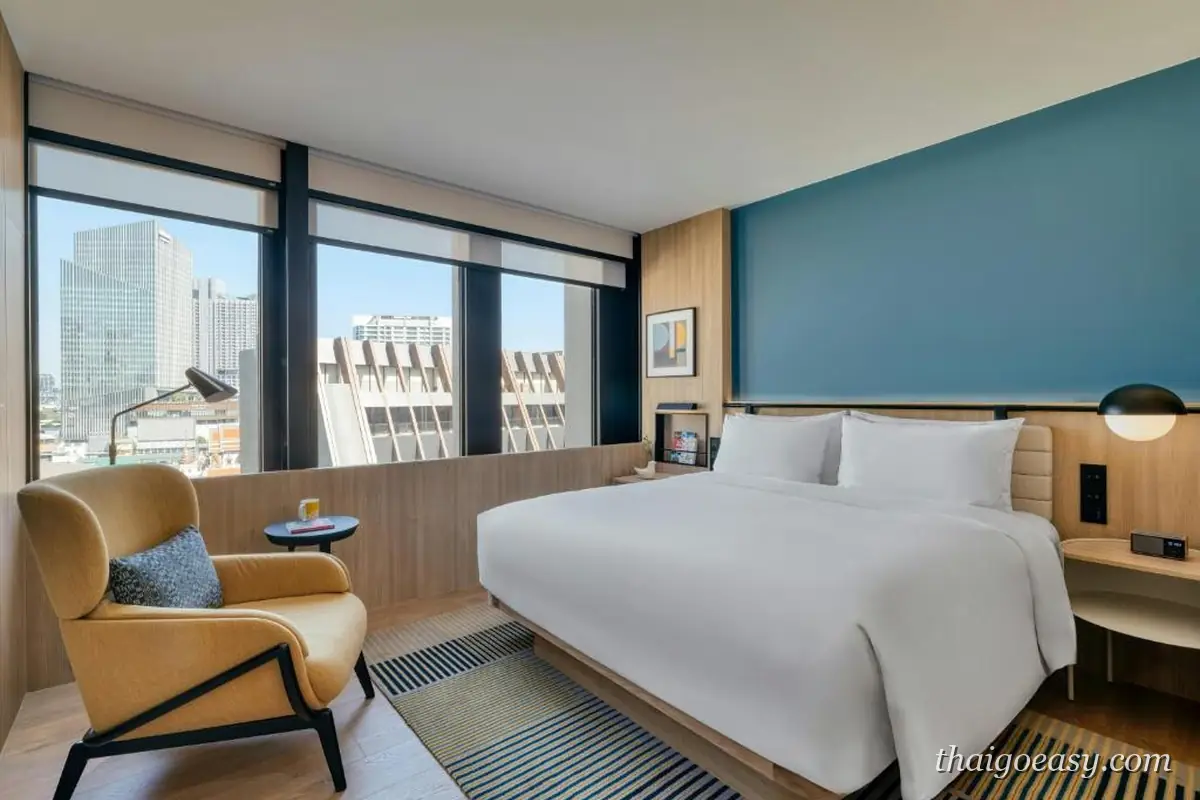 voco Bangkok Surawong 客房，藍色牆面、大床與窗邊黃色扶手椅