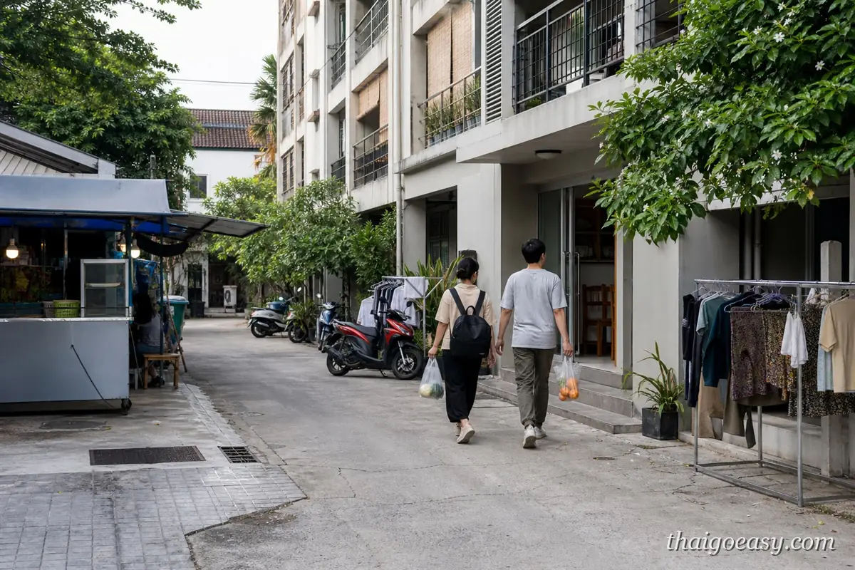旅客提著採買的塑膠袋走在清邁 Santitham 的公寓巷弄，路邊有小吃攤與曬衣架