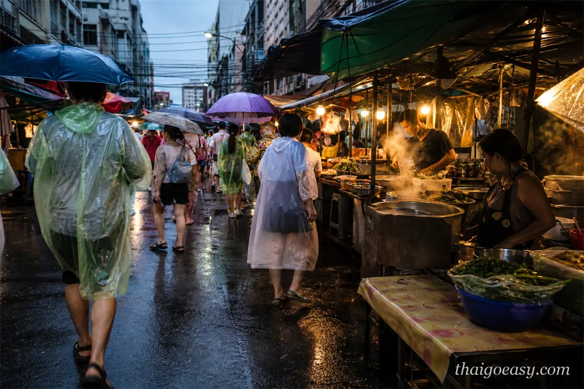 雨中的曼谷街邊小吃市集，穿雨衣的行人與冒著蒸氣的攤位