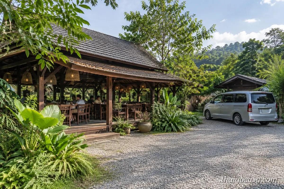 清邁郊區的木造開放式餐廳，客人坐在木桌用餐，屋外碎石地停著一台銀色廂型車，背景是樹林與山丘