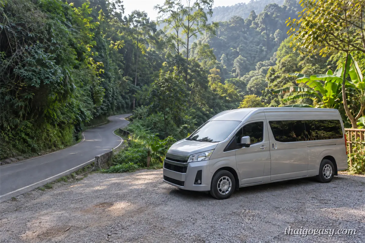 銀色廂型車停在往湄康蓬的山路旁碎石空地，前方是急彎的柏油山路與森林山谷