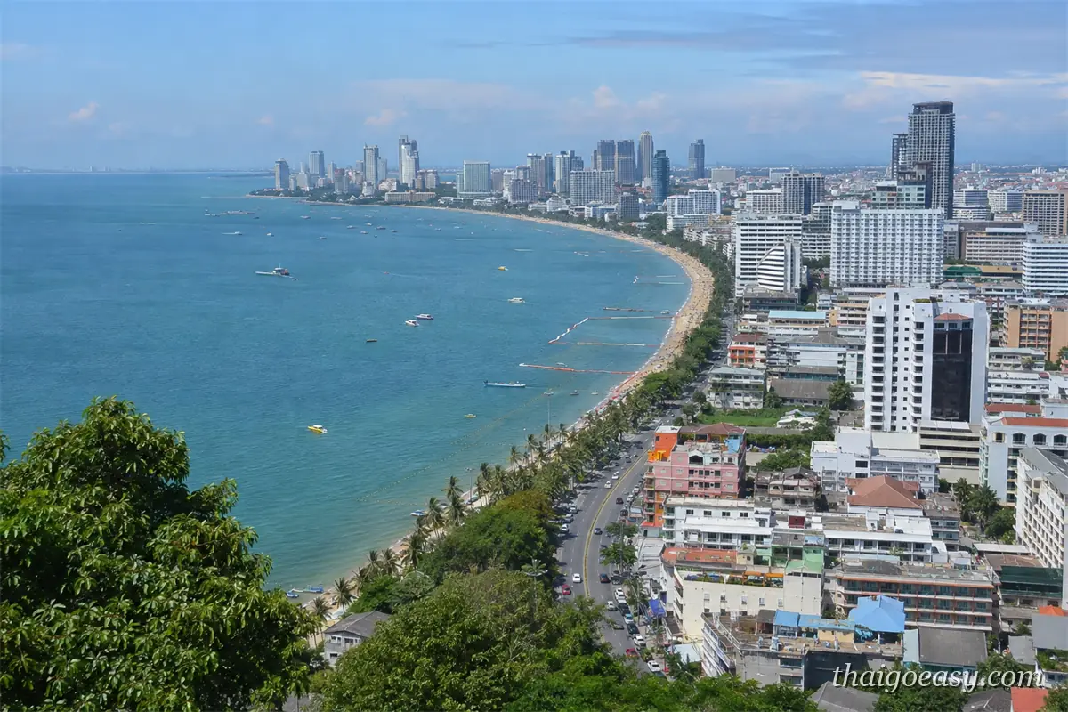 從高處俯瞰芭達雅海灣的完整弧線，沙灘沿岸是成排高樓與海濱道路，海面有多艘快艇