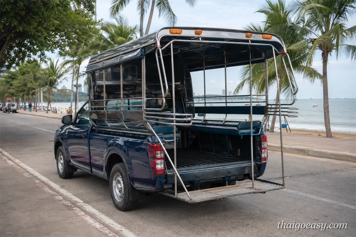 深藍色皮卡改裝的雙條車停在芭達雅海濱路旁，後方車廂是敞開式雙排座椅，路旁是椰子樹與沙灘