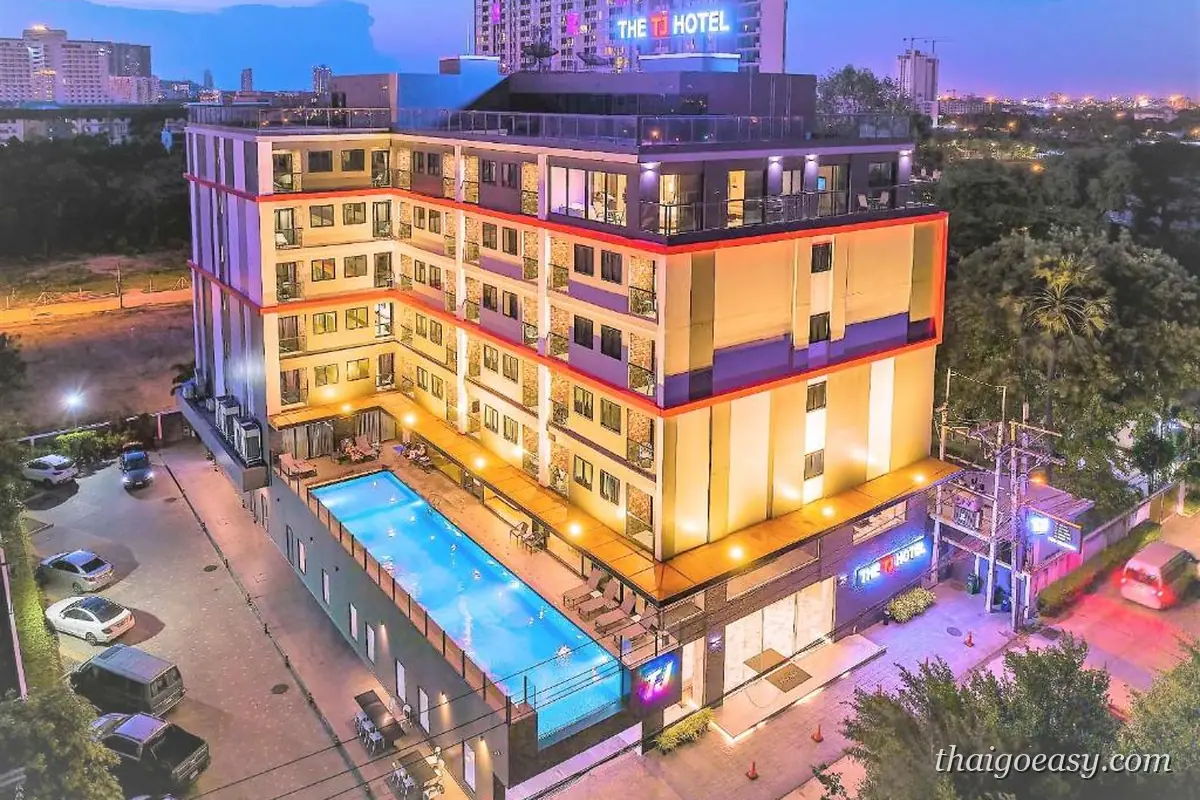 THE TJ HOTEL Pattaya 夜間空拍，中庭長型泳池亮著燈，樓頂有飯店霓虹招牌