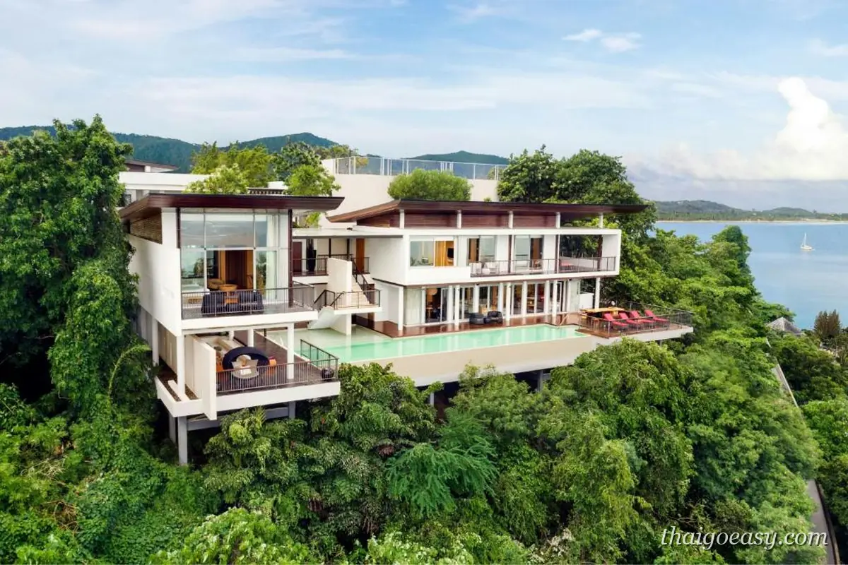 W Koh Samui 蓋在崖上的獨棟玻璃帷幕別墅，多層露台與長型泳池懸在樹林上方，遠方是海灣
