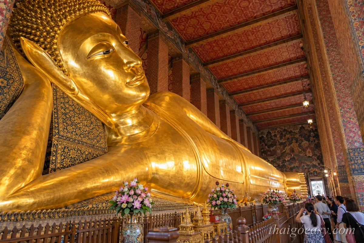 臥佛寺大殿內長 46 公尺、通體貼滿金箔的臥佛像，右側可見參觀的遊客與彩繪梁柱