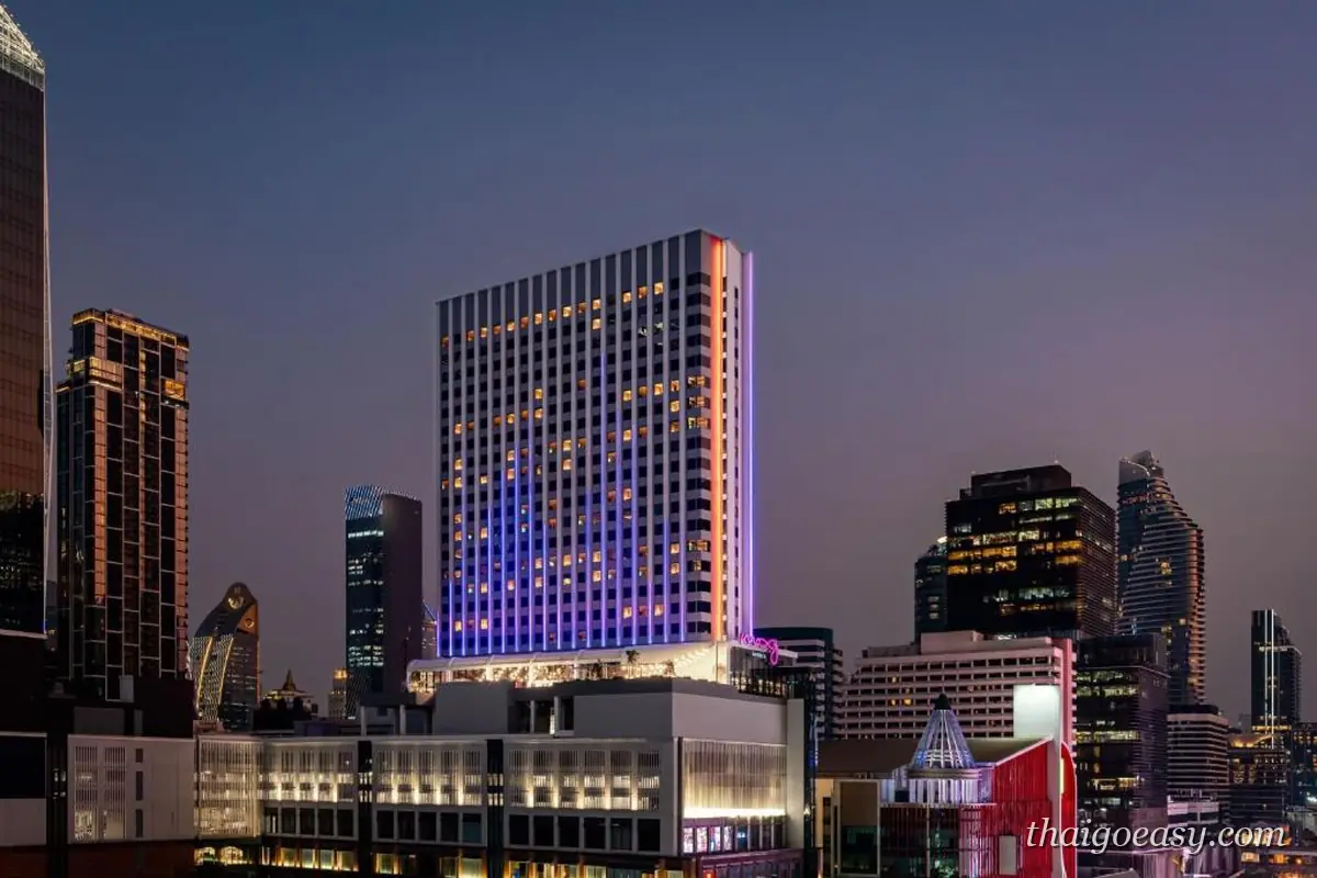 曼谷拉差巴頌 Moxy 酒店夜景，方形高樓立面打上紫色燈光，底層有粉色招牌